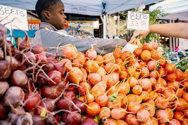 Vente directe sur un marché de producteurs Étal de fruits et légumes tenu par un producteur sur un marché fermier